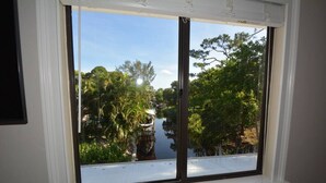 A window with a view of a water body, trees, and a building. - Canal View 2BR Retreat, Near Bonita Beach! Sleeps 4 (Bonita Springs)