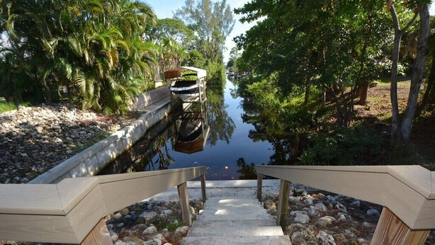 A wooden staircase leading down to a body of water, surrounded by trees and rocks. - Canal View 2BR Retreat, Near Bonita Beach! Sleeps 4 (Bonita Springs)