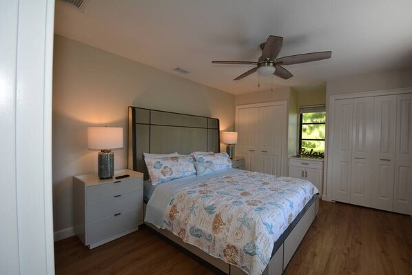 Un dormitorio con cama, mesitas de noche, ventilador de techo y ventana con vistas.