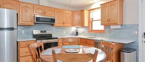 Une cuisine moderne avec des meubles en bois, des appareils électroménagers en acier inoxydable et un coin repas comprenant une table ronde et des chaises.