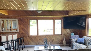 Un salon avec un plafond en bois, une grande fenêtre, un canapé, un téléviseur et une petite table sur laquelle sont posés un vase et une sculpture.