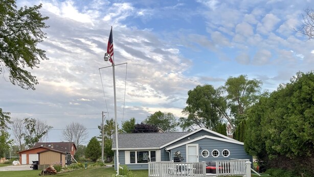 Une maison avec une jetée qui s’avance sur une étendue d’eau, un mât portant le drapeau américain et une clôture blanche en bois.