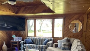 Un salon chaleureux avec un plafond en bois, une grande fenêtre, un téléviseur à écran plat et un canapé agrémenté de plusieurs coussins.