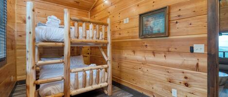 A wooden cabin with bunk beds, a framed picture on the wall, and a window with blinds.