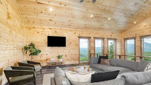 Een houten cabin interieur met een grote bank, fauteuils, een televisie en een tafel met drankjes.