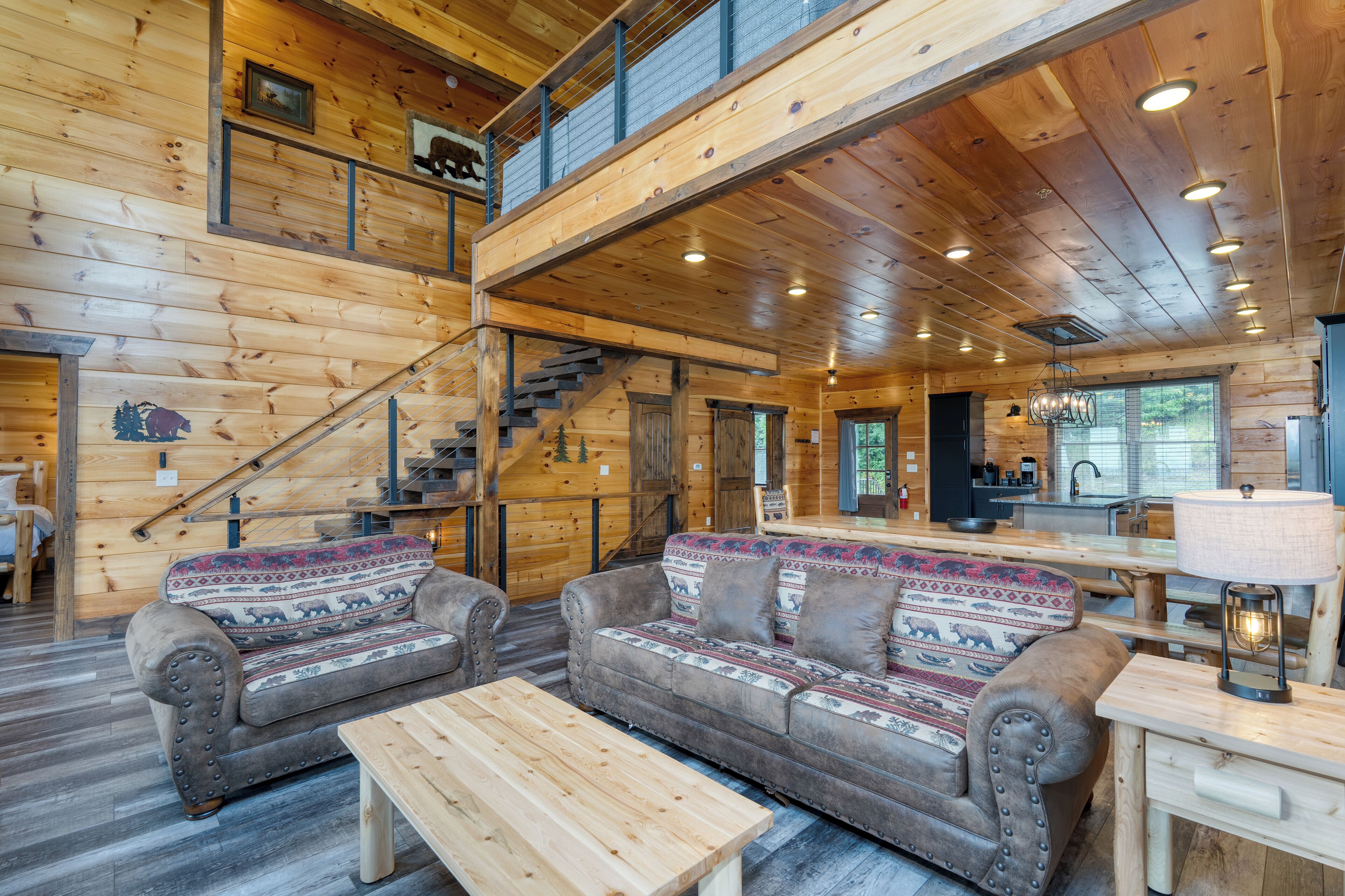 A log cabin interior with a loft bedroom, a dining area, and a living room with two sofas and a coffee table.