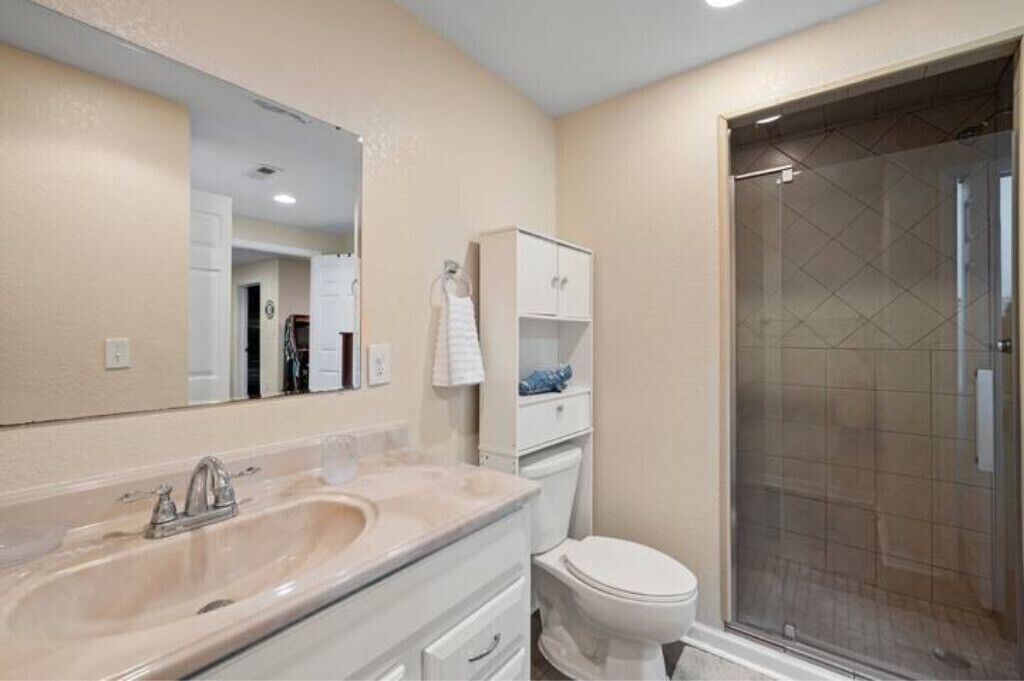 A bathroom with a large mirror, a sink, a toilet, and a glass-enclosed shower.