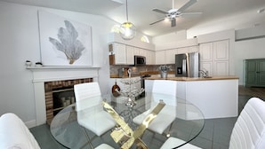 A modern kitchen with white cabinetry, a central island, and a dining area with a glass table and white chairs. - Private Heated Pool and Hottub , Pet Friendly, New Golf Cart , Close to shopping (Lady Lake)