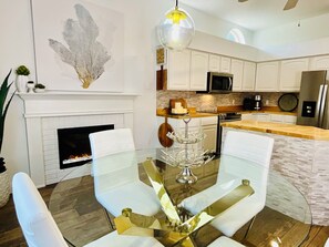 A modern kitchen with white cabinetry, a fireplace, and a dining area with a glass table and white chairs. - Private Heated Pool and Hottub , Pet Friendly, New Golf Cart , Close to shopping (Lady Lake)