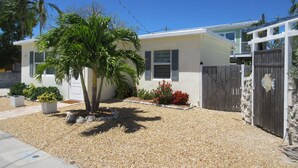 A single-story house with a gravel driveway, a palm tree, and a wooden fence. - Private Pool & Dock (Marathon)