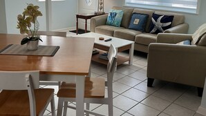 A living room with a dining table, chairs, a sofa, and a coffee table. There are decorative fish on the wall, a lamp, and a window with blinds. - Private Pool & Dock (Marathon)