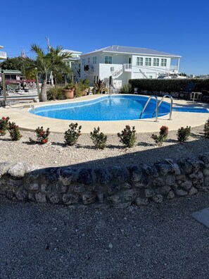 A swimming pool with a stone wall in the foreground, a white building in the background, and a clear blue sky.