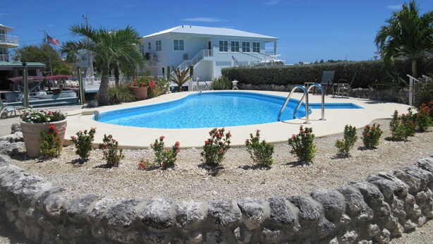 A swimming pool surrounded by a stone wall, with a white building in the background. - Private Pool & Dock (Marathon)