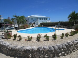 A swimming pool surrounded by a stone wall, with a white building in the background. - Private Pool & Dock (Marathon)