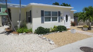 A single-story house with a white exterior, a front door with a circular window, and a small front yard with gravel and plants. - Private Pool & Dock (Marathon)