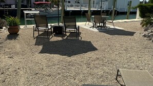 An outdoor seating area with tables and chairs, a potted plant, and a view of a marina with boats and buildings in the background. - Private Pool & Dock (Marathon)