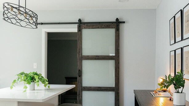 Een moderne keuken met een centraal kookeiland, donkerhouten stoelen, een hangende lamp en een schuifdeur in boerderijstijl.