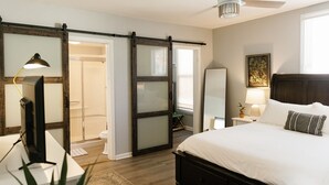 Een slaapkamer met een bed, nachtkastje, lamp en een schuifdeur naar een badkamer.