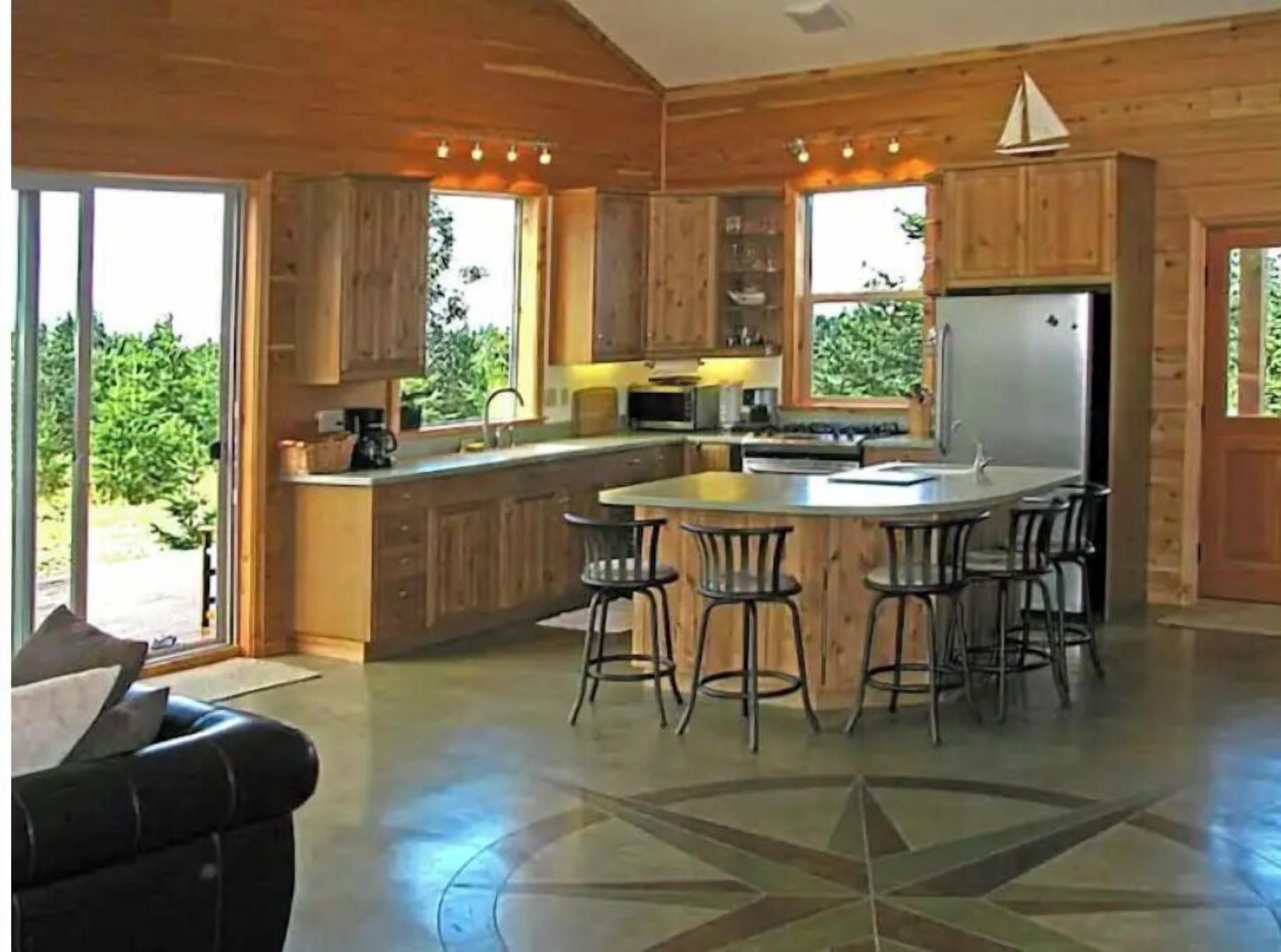 A modern kitchen with wooden cabinets, a central island with bar stools, and a large refrigerator.