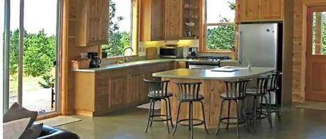 A modern kitchen with wooden cabinets, a central island with bar stools, and a large refrigerator.