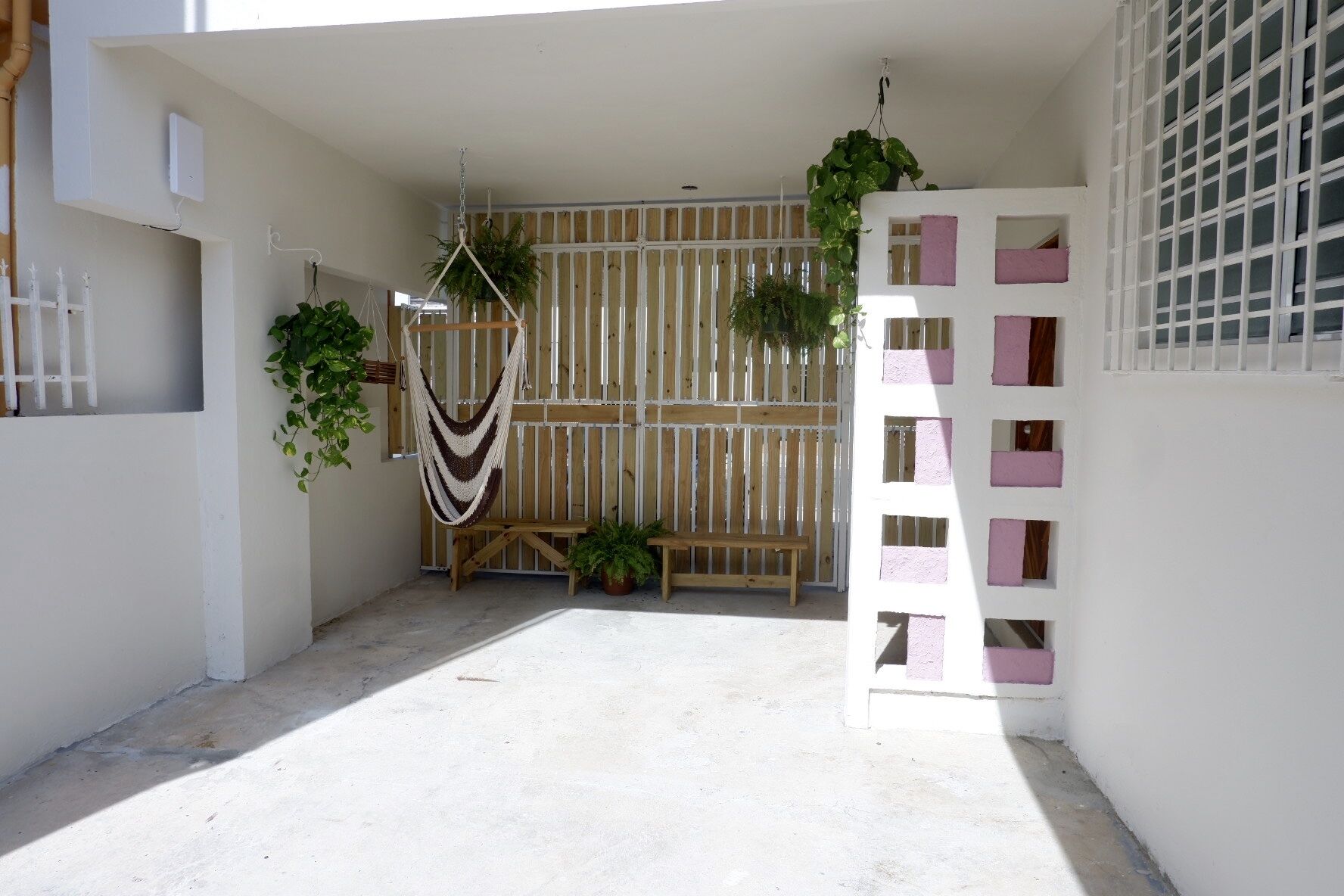 Un espacio al aire libre cubierto con un banco de madera, plantas colgantes y una valla blanca.