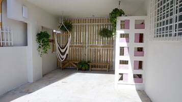 Un espacio al aire libre cubierto con un banco de madera, plantas colgantes y una valla blanca.