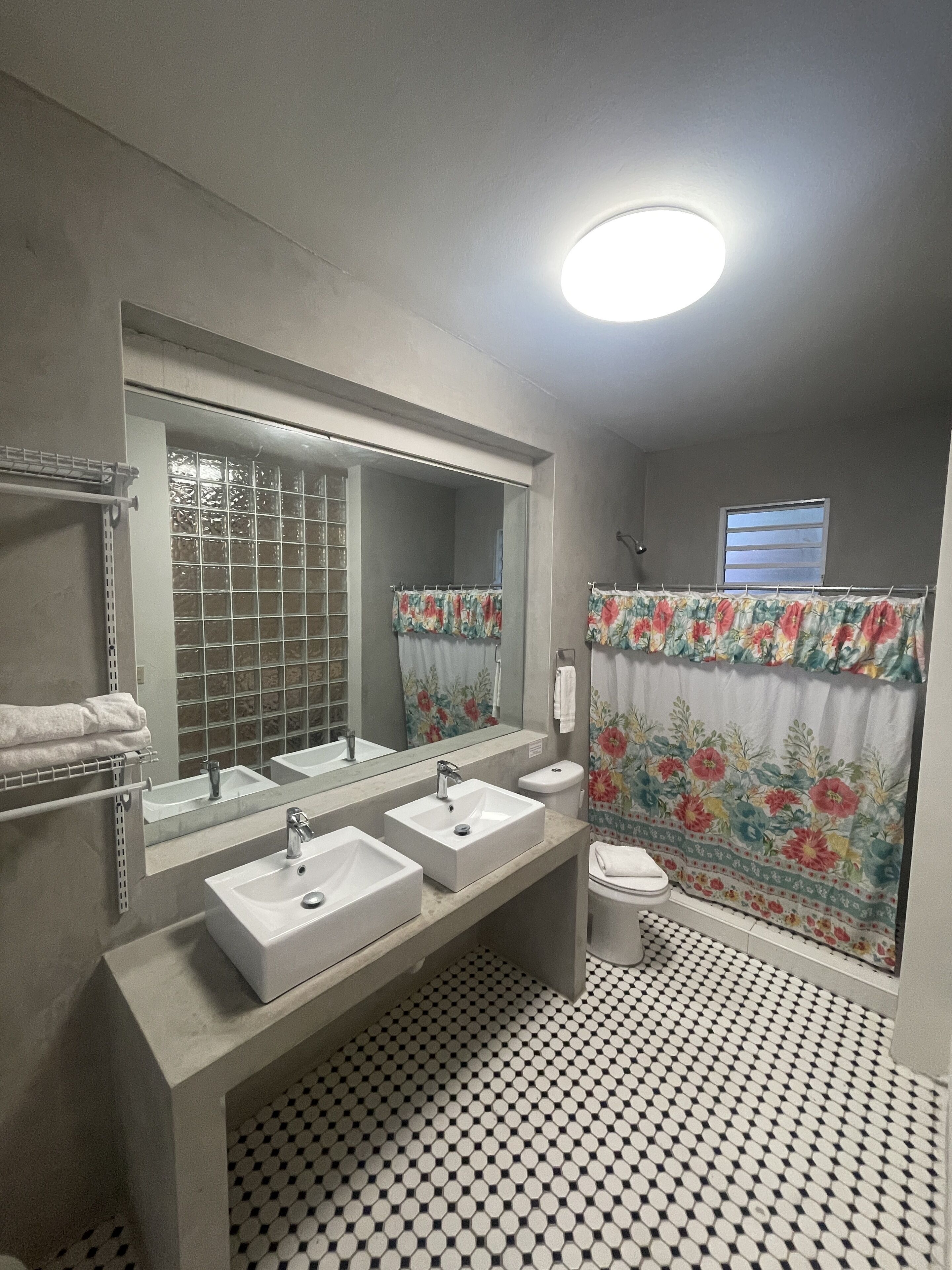 A bathroom with two sinks, a toilet, a shower with floral curtains, a large mirror, and a patterned floor.