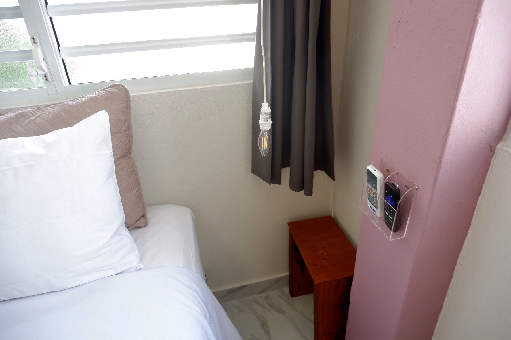 A hotel room with a bed, a small wooden nightstand, a wall-mounted phone, and a window with curtains.