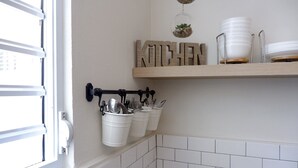 A kitchen with a wooden shelf holding plates and a wall-mounted utensil holder with pots and pans. - The Emerald (San Juan)
