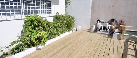 Une terrasse en bois avec un mur blanc et une fenêtre ornée de barreaux en métal.