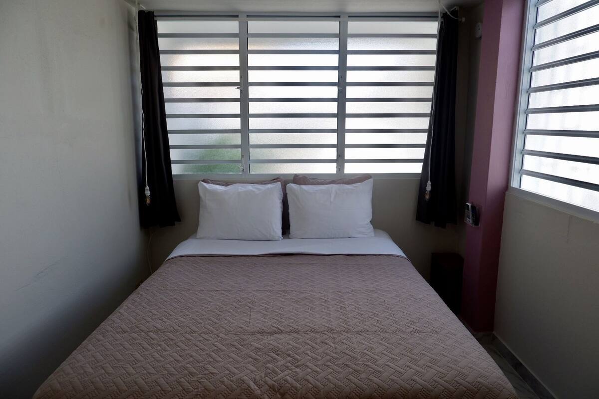 Quarto pequeno com uma cama de solteiro, janela e porta.