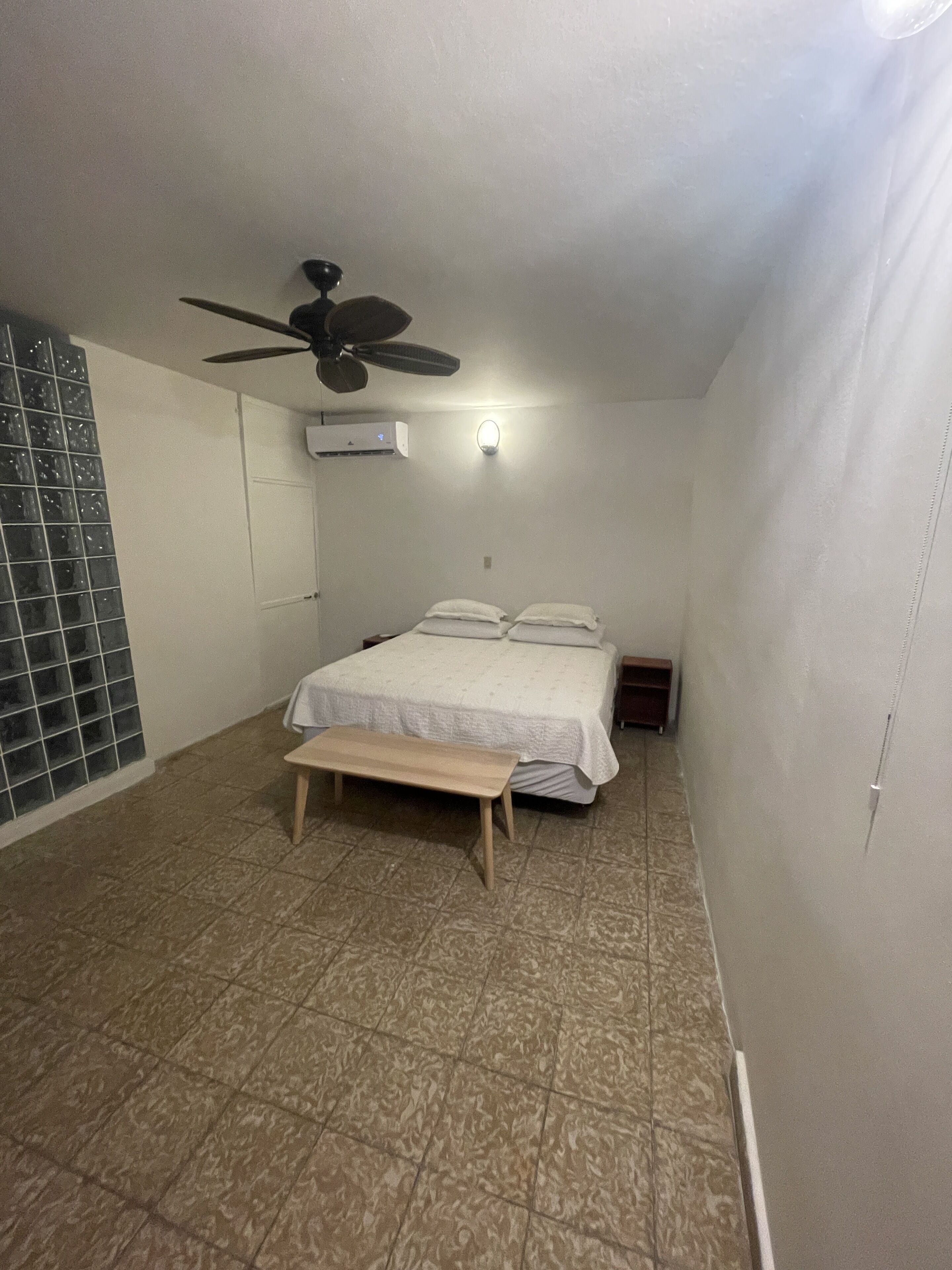 Ein Schlafzimmer mit einem Bett, einem Deckenventilator, einer Klimaanlage und einer Bank.