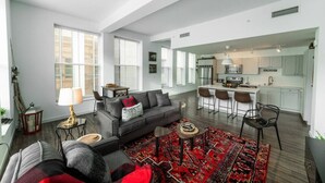 A spacious living area with a sofa, coffee table, and a red patterned rug. There is a kitchen area with a bar and seating. - 725- Big 2 bedroom/king beds/Corner Unit/ + parking (Milwaukee)