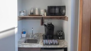 Eine kompakte Küche mit Spüle, Mikrowelle, Kaffeemaschine, Toaster und kleinem Kühlschrank.