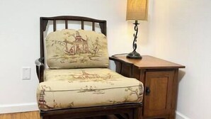 Una silla con cojín estampado con un diseño de paisaje, un pequeño armario de madera y una lámpara de mesa.