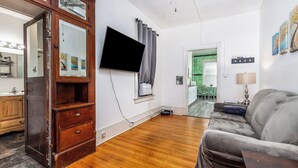 Una sala de estar con un aparador de madera, un televisor de pantalla plana, un sofá gris y un comedor con una mesa y sillas verdes.