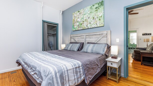 Un dormitorio con cama, mesitas de noche, un ventilador y un cuadro en la pared.