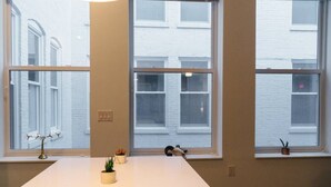 A modern room with a long white table, three windows, and small potted plants.