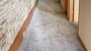 Un pasillo con pared de ladrillo, piso alfombrado y puertas de madera.