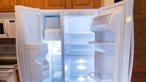 Un refrigerador abierto con múltiples estantes y un compartimento congelador, ubicado en una cocina con armarios de madera y un microondas.