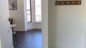 A room with a dark wooden floor, a bench with a patterned cushion, a coat rack, and a framed picture on the wall.