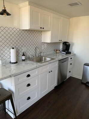 A kitchen with white cabinets, a marble countertop, a coffee maker, and a sink.