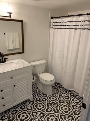 A bathroom with a white toilet, a sink with a mirror, and a patterned floor.