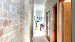 A corridor with a brick wall on one side and wooden doors on the other. - Unit C- New Big 2 King Bedroom Condo by FiservForum/3rd St (Milwaukee)