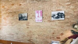 A cozy seating area with a brick wall, a white sofa, and two small tables. - Unit C- New Big 2 King Bedroom Condo by FiservForum/3rd St (Milwaukee)