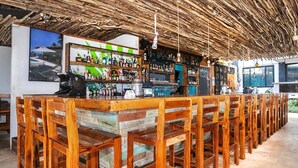 Zona de bar con sillas de madera y techo de paja.