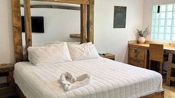 Um quarto espaçoso com uma cama grande, cabeceira de madeira, ventilador de teto, uma escrivaninha e uma janela com luz natural.