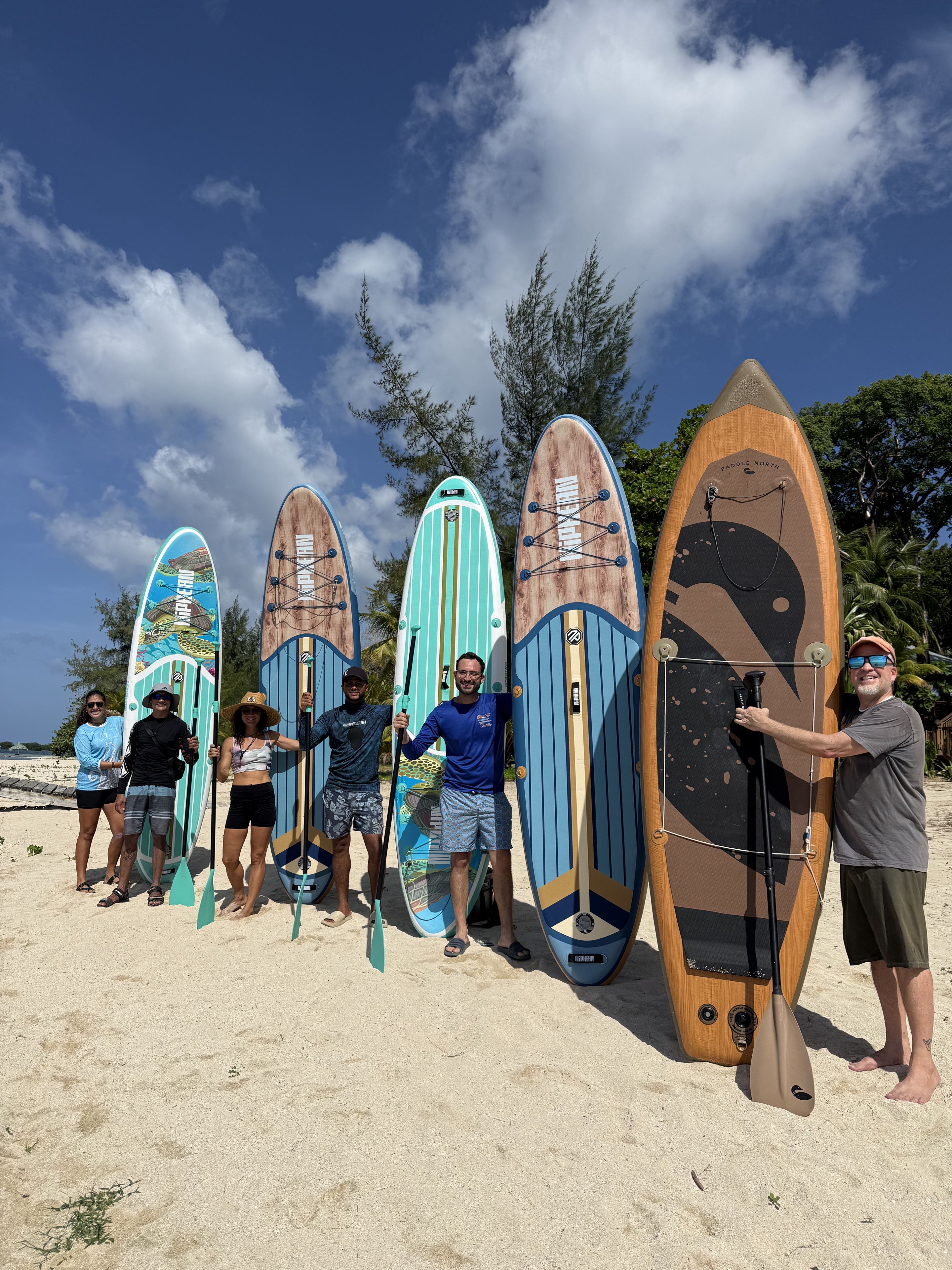 A group of people standing on a sandy beach with paddleboards.