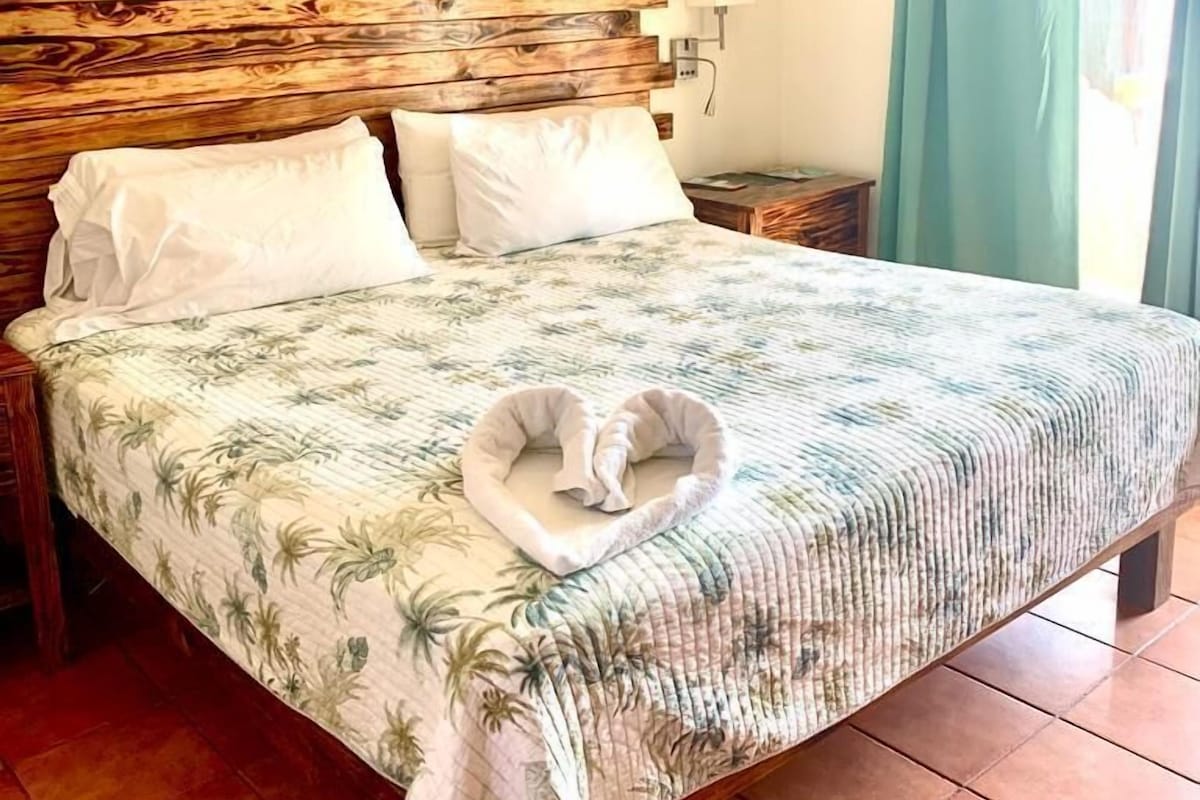 A bed with a floral bedspread, a heart-shaped pillow, and a towel on the floor.