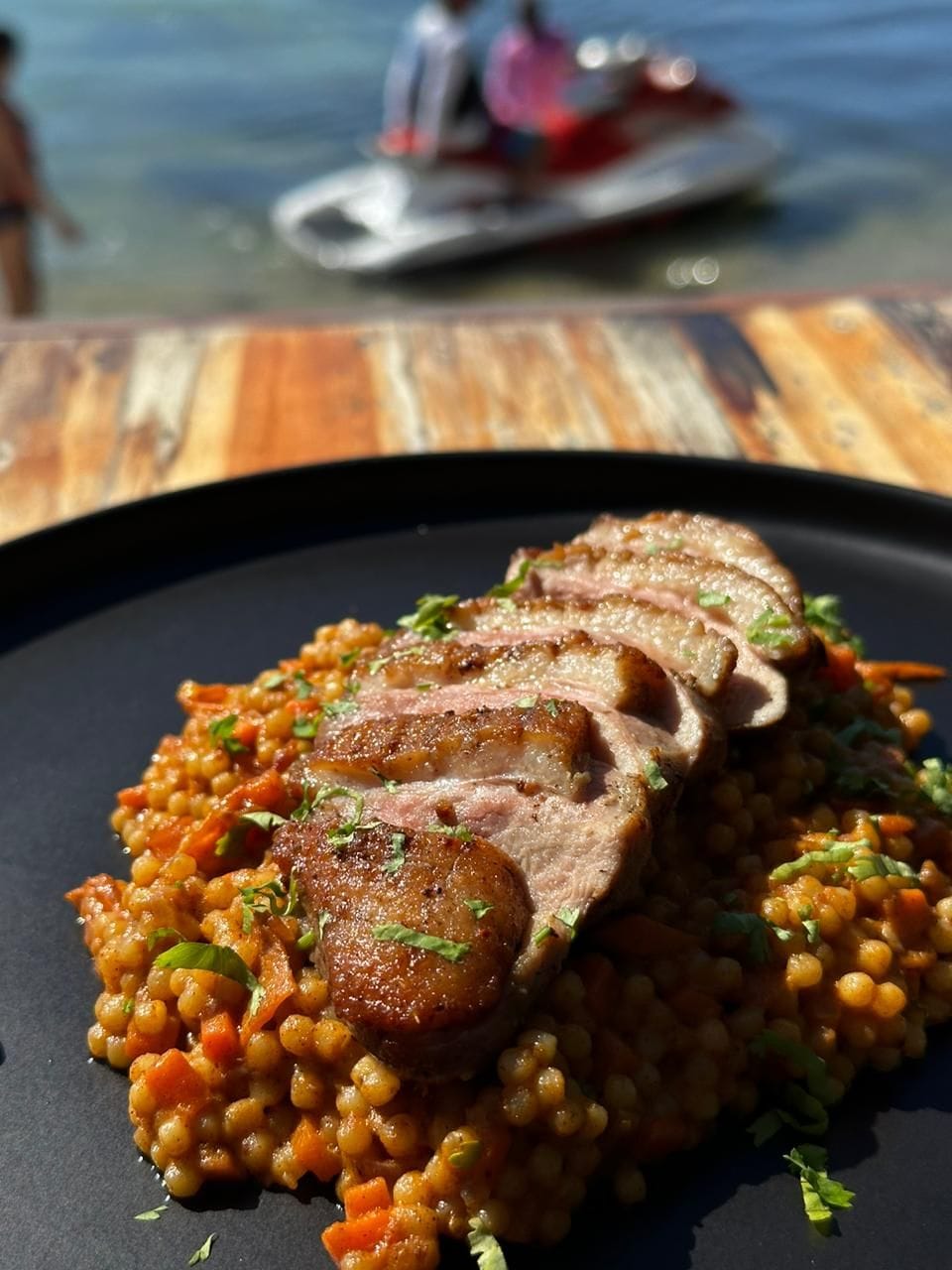 Ein Teller mit Essen, darunter geschnittenes Fleisch und Linsen, vor einem unscharfen Hintergrund eines Holztisches.